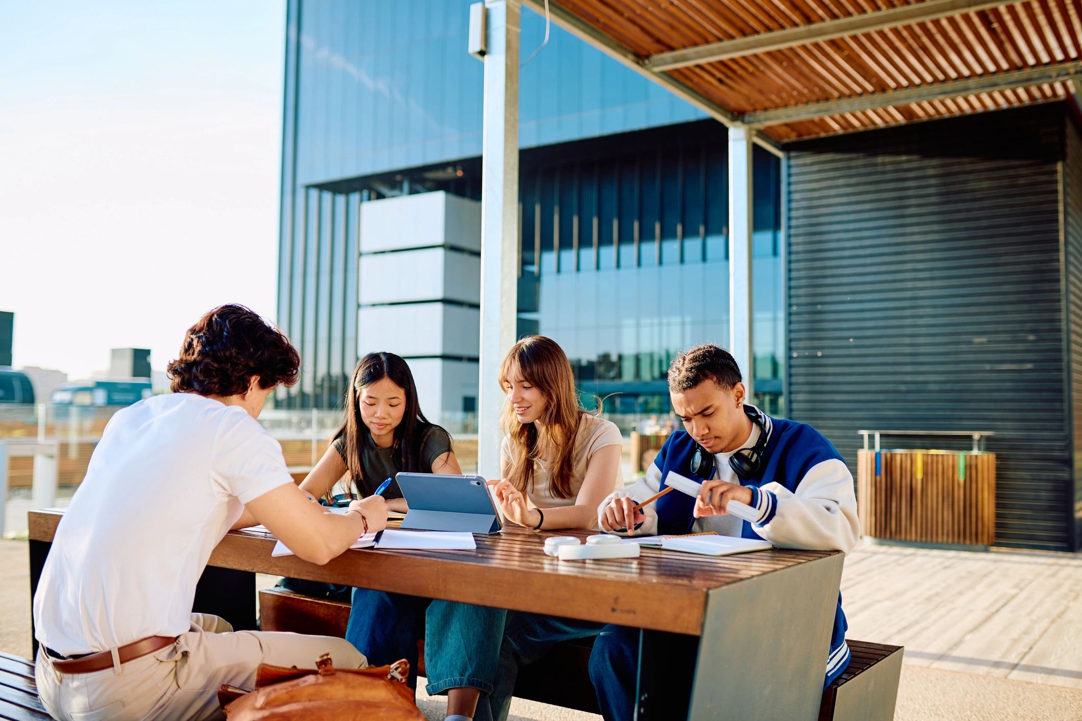 Diverse group of university students studying and working together at an outdoor table on modern campus